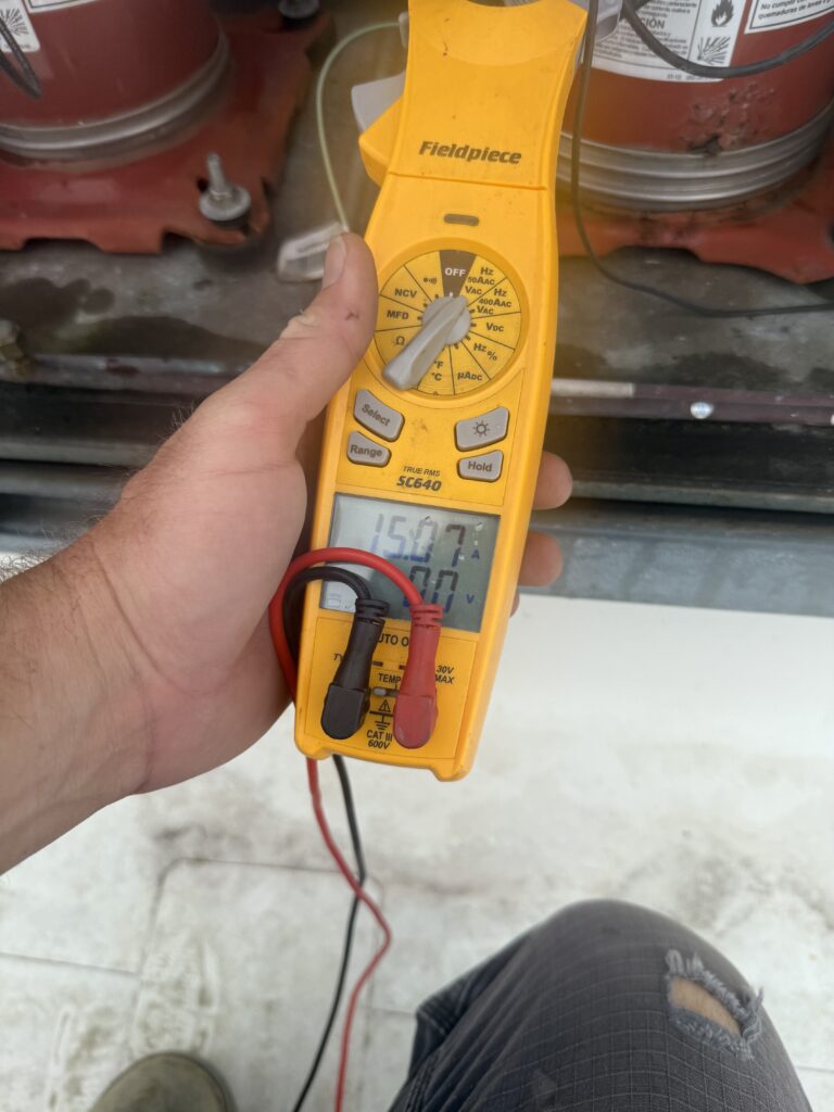 Extreme Temp technician testing commercial rooftop unit electrical components with a Fieldpiece clamp meter