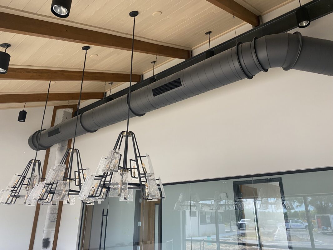 Long run of black spiral metal ductwork installed alongside pendant lighting in a new construction office in Southwest Florida