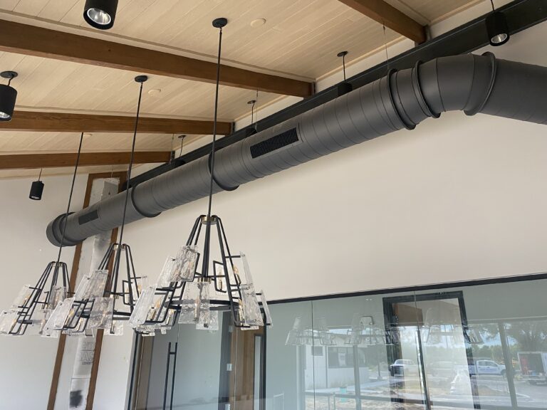 Long run of black spiral metal ductwork installed alongside pendant lighting in a new construction office in Southwest Florida