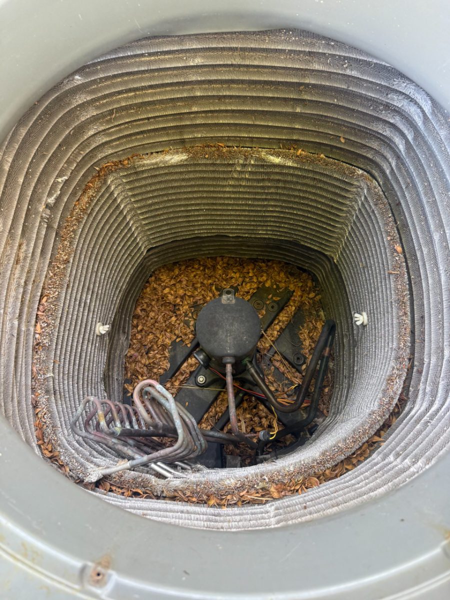 Leaves and debris trapped in the base of an outdoor AC condenser around the compressor, which holds moisture and leads to corrosion